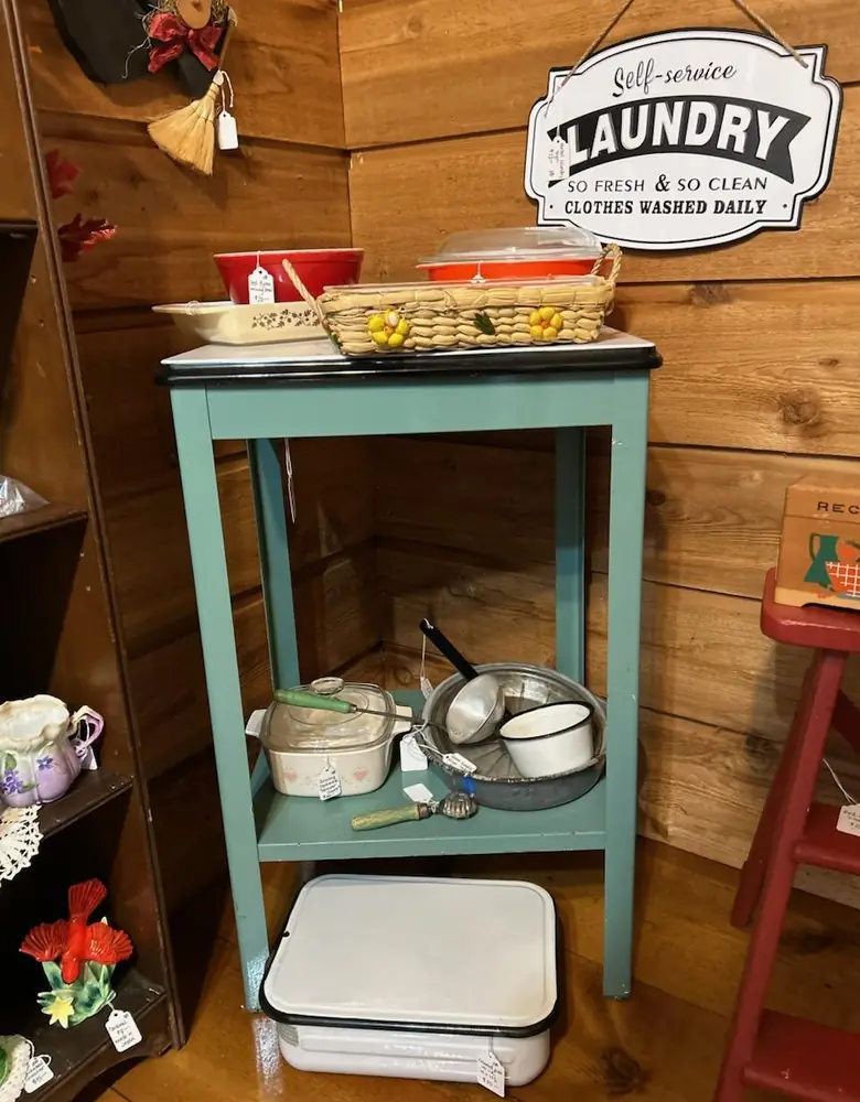 Teal side table with enamelware and a vintage laundry sign inside Chaintiques
